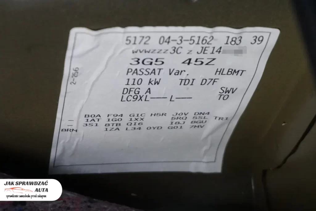 Biała naklejka serwisowa (wlepka) w bagażniku VW z kodami wyposażenia, kodem lakieru i numerem VIN.